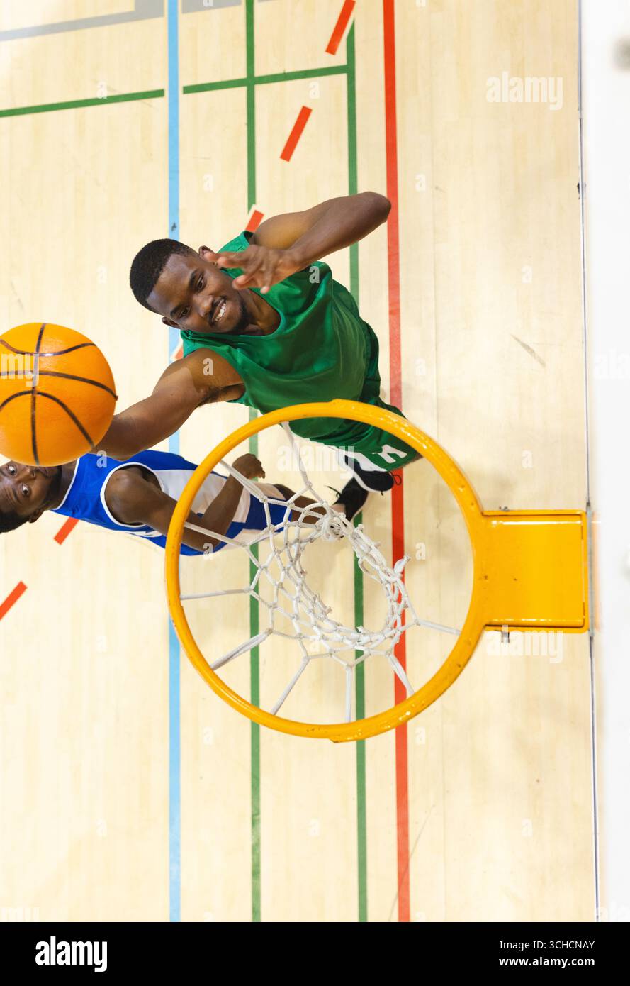 Uomini afroamericani che saltano sul campo da ginnastica verso il bordo del cerchio e la rete bianca che regge il basket. Atletica, competizione, movimento, squadra, sport, dinamico, Foto Stock