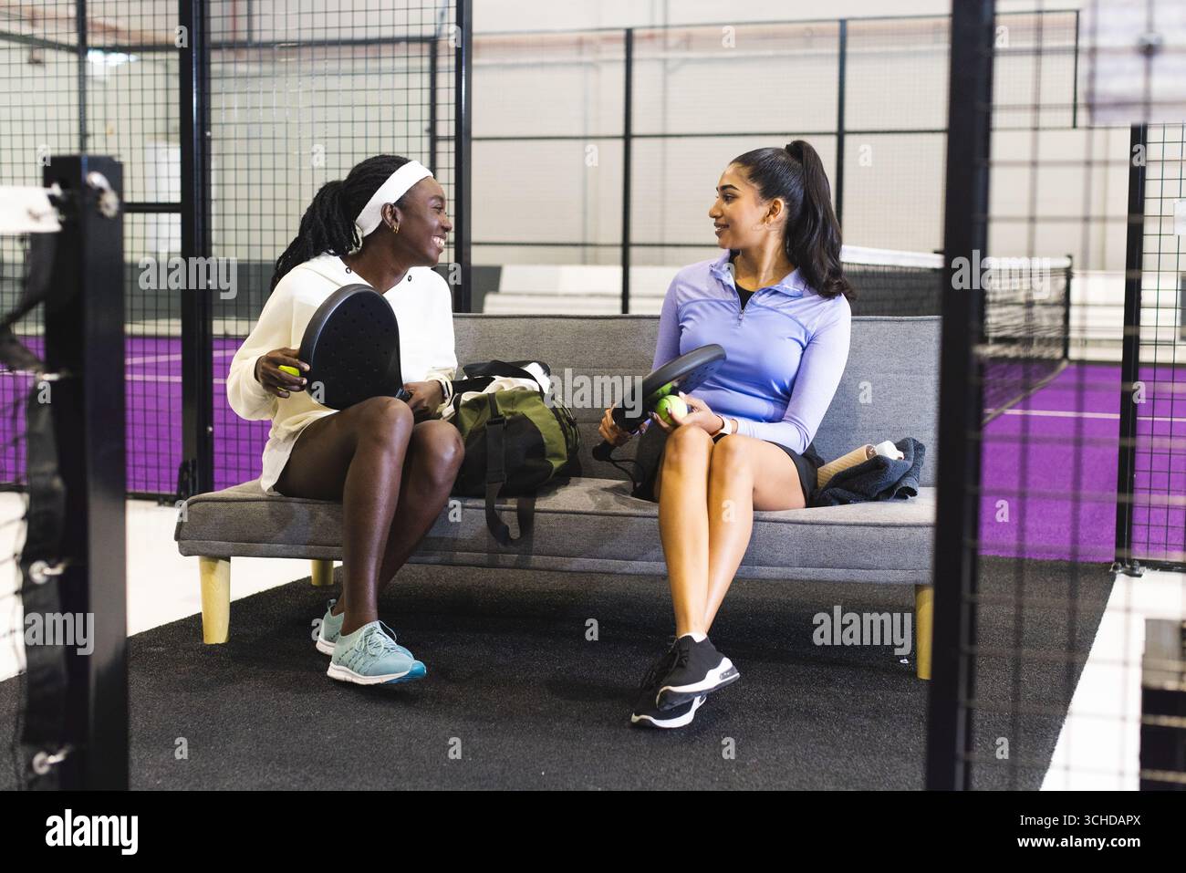 Diverse amiche sedute sulla panchina accanto al campo da padel con racchette e palle in borsa sportiva Foto Stock
