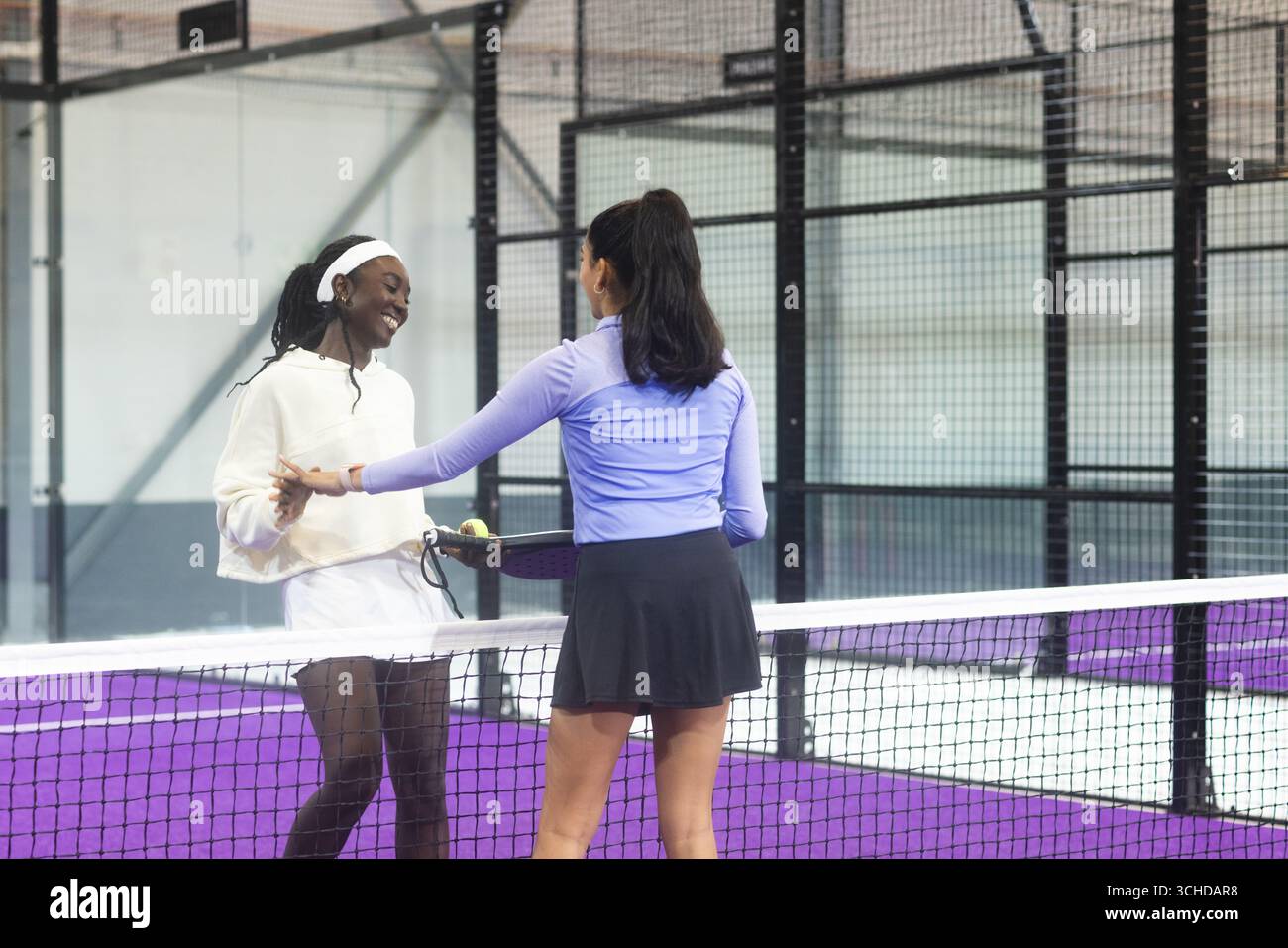 Diverse giocatrici di padel femminili con racchette che stringono le mani su una rete sul campo in un recinto a rete Foto Stock