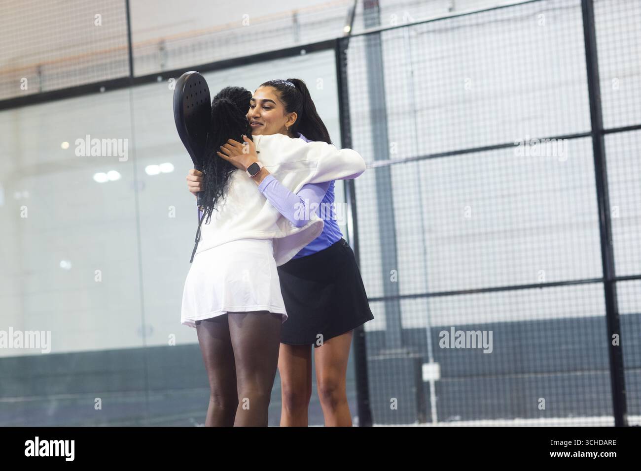 Diverse atlete che si abbracciano vicino alla rete sul campo del padel dopo la partita con le racchette del padel Foto Stock