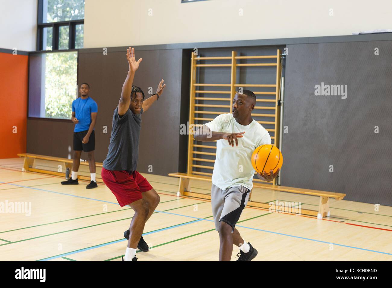 Amici afroamericani che dribblano basket nella palestra scolastica con panca, bottiglia d'acqua Foto Stock