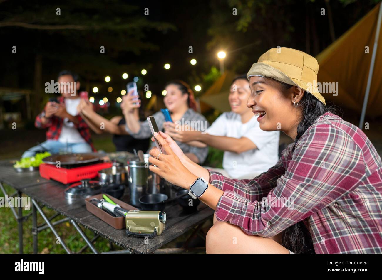 Gli indonesiani del sud-est asiatico si godono un campeggio di notte, utilizzando i loro cellulari per catturare momenti e condividere esperienze. La scena della vita Foto Stock