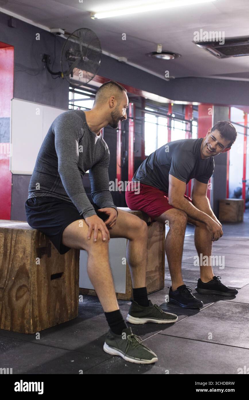 Diversi amici maschi che riposano su scatole plyometriche all'interno della palestra indossando abbigliamento atletico Foto Stock
