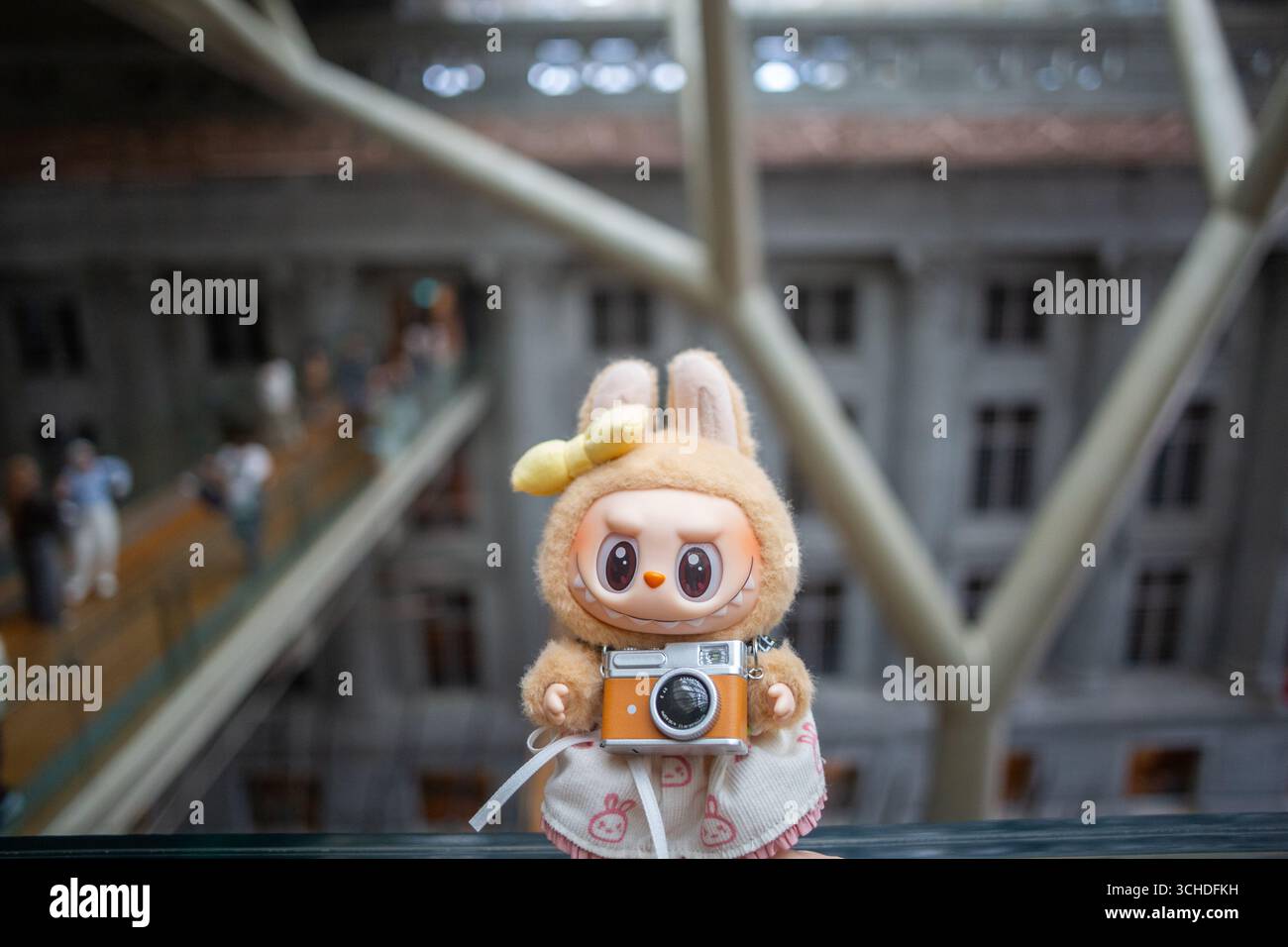 Tourist Labubu con una macchina fotografica e posa alla National Gallery di Singapore. Lei ama fare fotografia. Nastro giallo sulla sua testa. Foto Stock