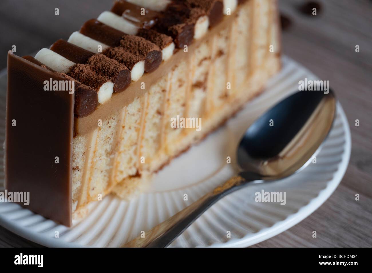 Primo piano di una fetta di torta a strati di cioccolato e panna su un piatto bianco con un cucchiaio, evidenziando le ricche consistenze della torta e l'appagante glassa Foto Stock
