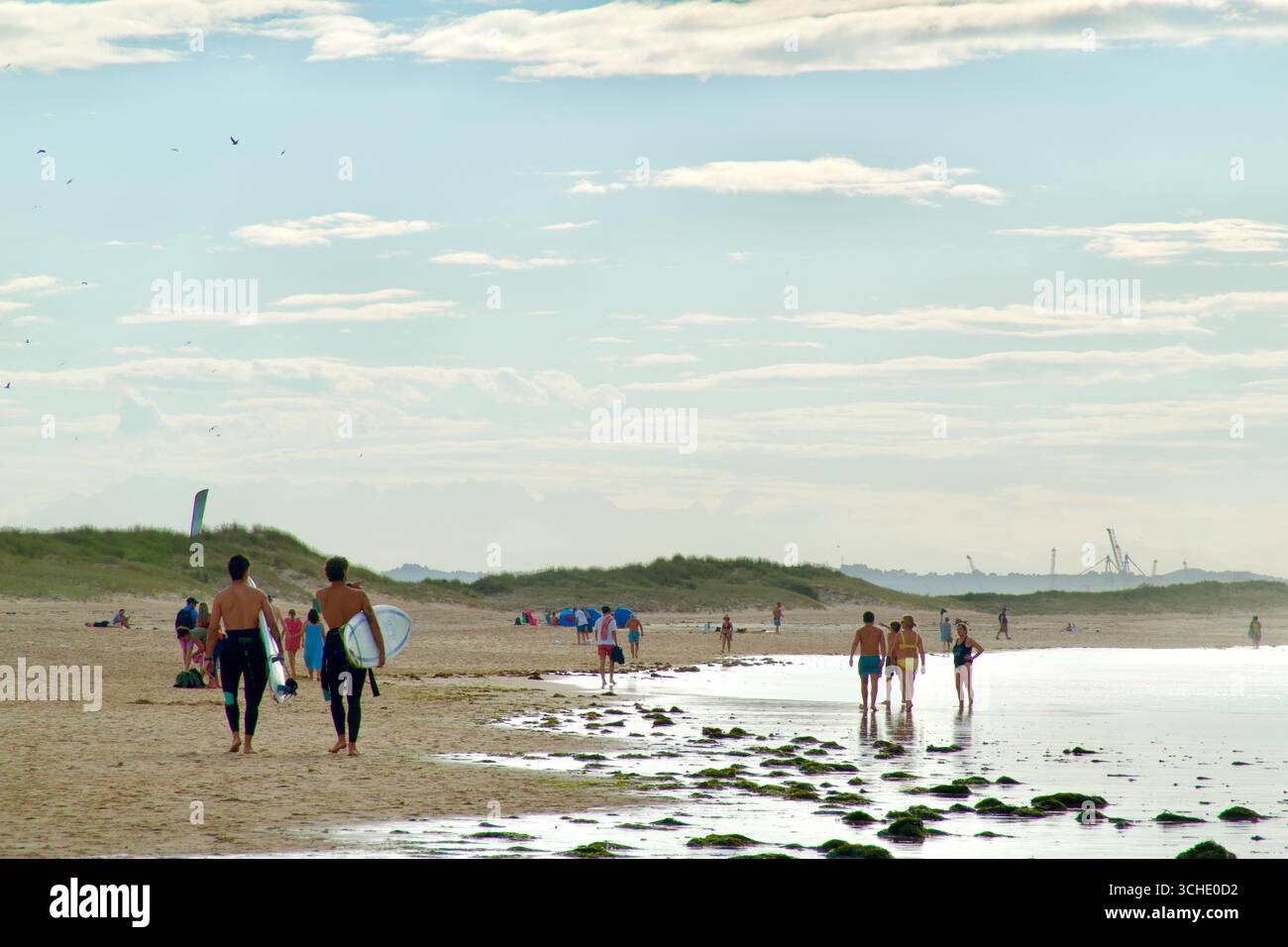 Due giovani uomini che trasportano tavole da surf e turisti in una serata estiva sulla spiaggia di Somo famosa per il surf Ribamontan al Mar Cantabria Spagna Europa Foto Stock