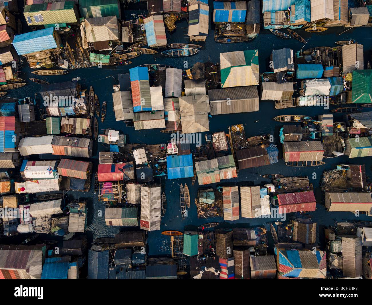 Vista aerea di una vivace e estesa comunità dove i tetti colorati incontrano le acque scure e riflettenti, creando un mosaico di vita e sostentamento. Lagos, Lagos, Nigeria. Foto Stock