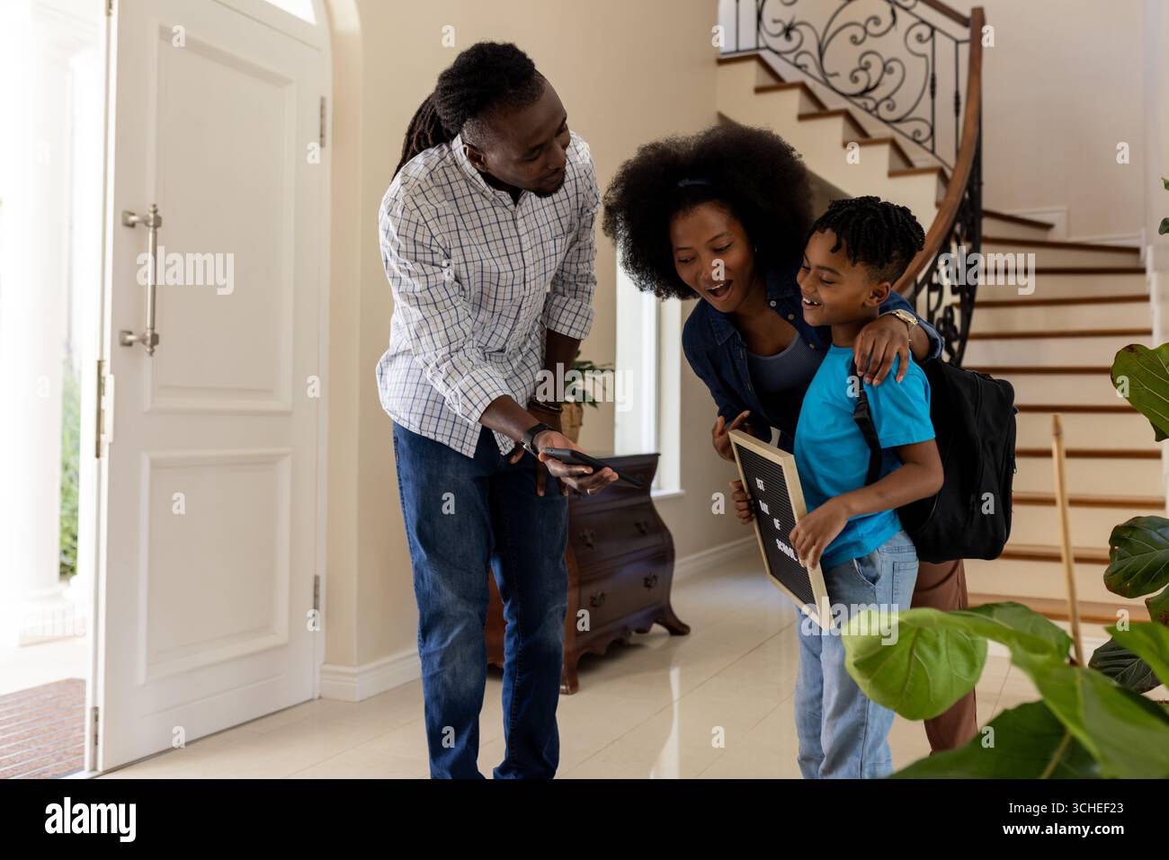 Genitori afroamericani che aiutano il figlio con zaino e tablet all'ingresso di casa Foto Stock