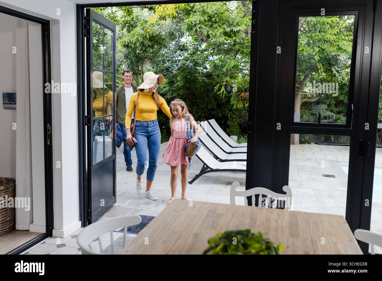 La famiglia entra a casa dal patio, sorridendo e godendosi una giornata di sole insieme Foto Stock