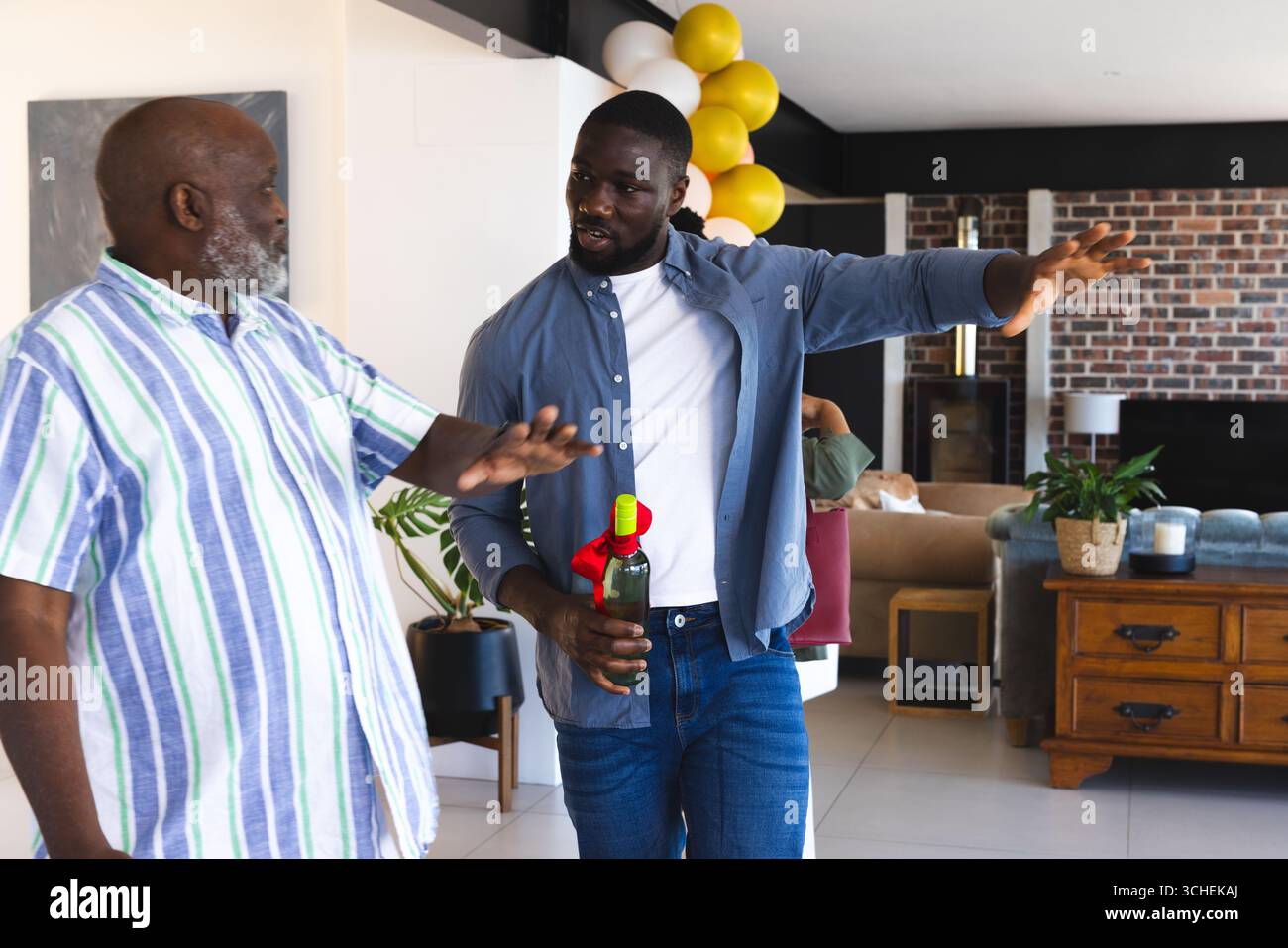 Due uomini in un abbigliamento informale discutono mentre tengono una bottiglia di vino a casa Foto Stock