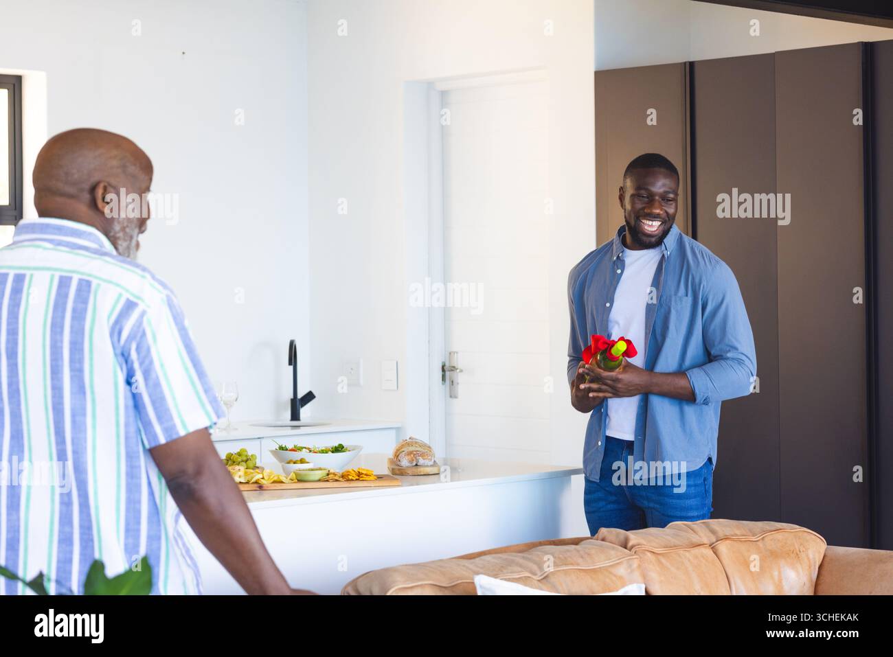 Uomo che tiene fiori sorridenti a un uomo anziano nella cucina moderna, festeggiando insieme Foto Stock