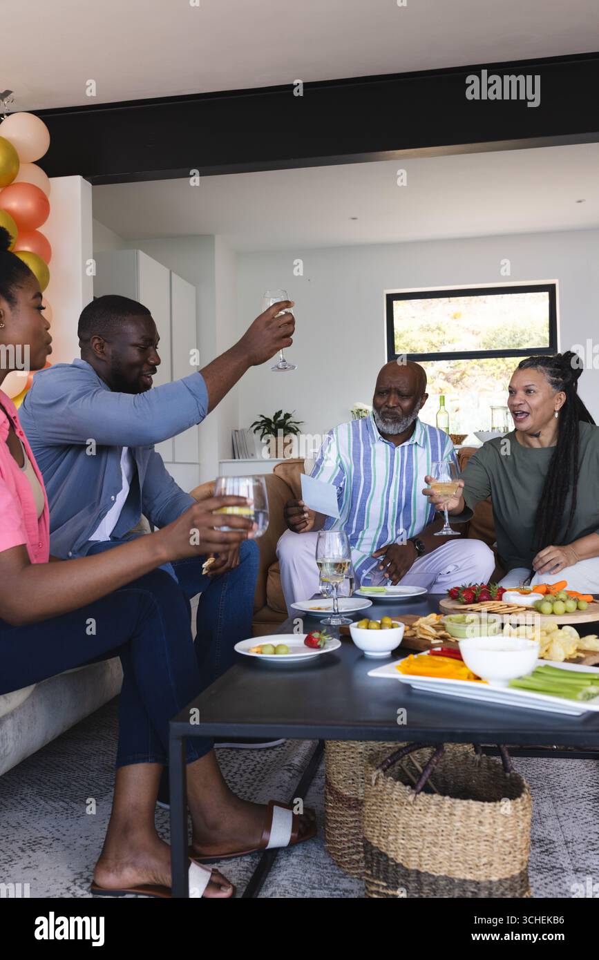 Gli amici brindano con bevande a casa, godendosi un incontro festoso con spuntini Foto Stock