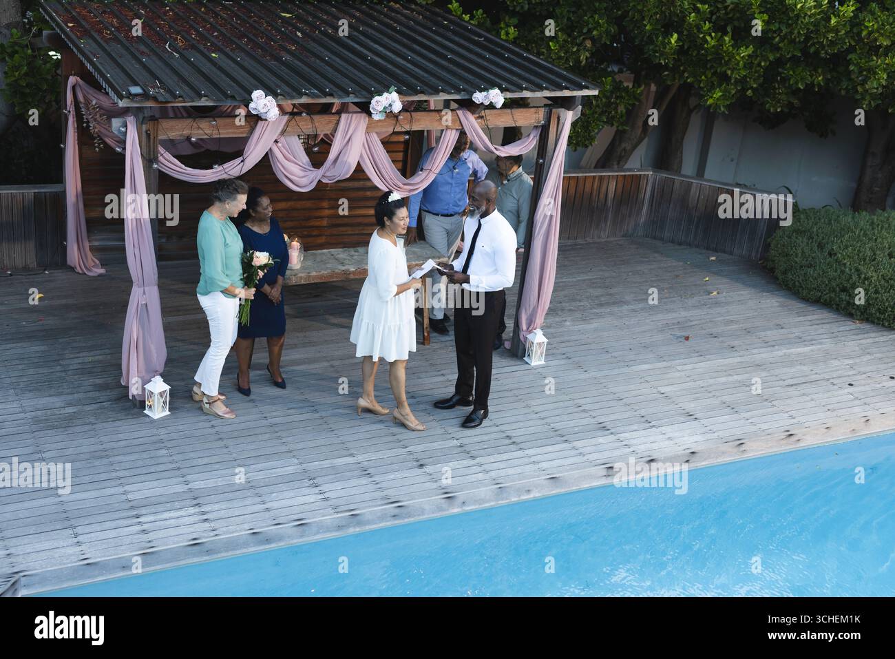 Coppia che si scambia le promesse a bordo piscina con gli amici per celebrare un'occasione gioiosa Foto Stock