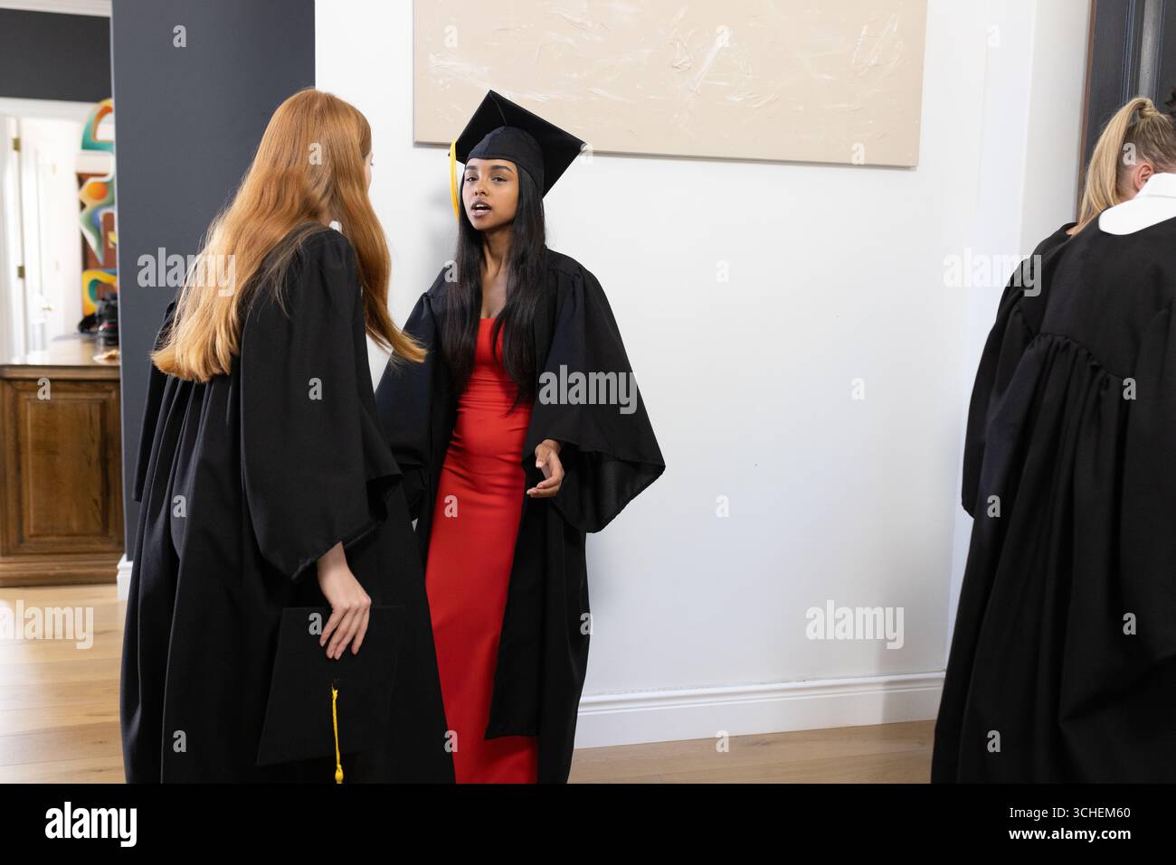 Laureati in berretti e camici che chiacchierano eccitatamente a casa dopo la cerimonia Foto Stock