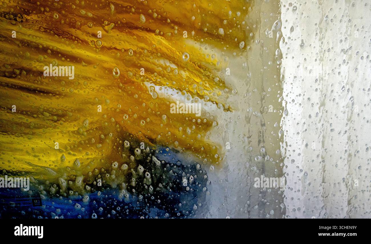 I colori brillanti si mescolano come spruzzi d'acqua da una lavatrice, lavando via lo sporco e la sporcizia dai veicoli durante una giornata di sole. Foto Stock