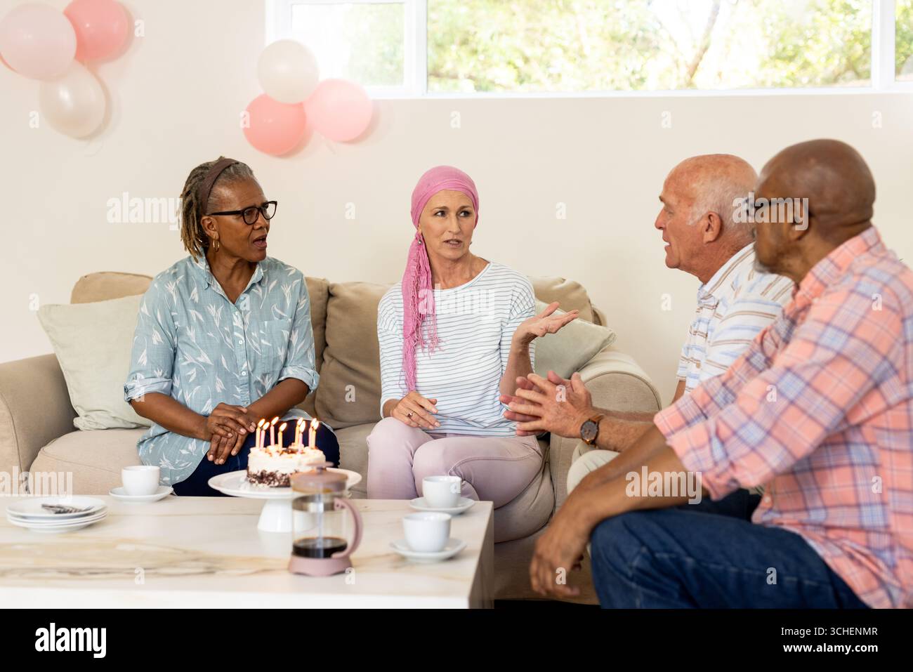 Amici anziani diversi che si godono la festa di compleanno con una torta e una conversazione a casa Foto Stock