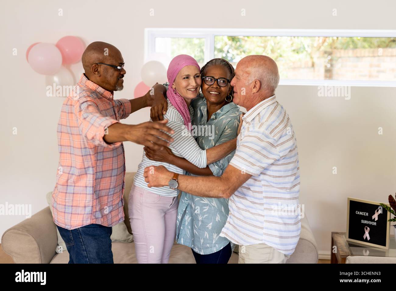 Amici anziani che accolgono e celebrano i sopravvissuti al cancro a casa, sorridendo con gioia Foto Stock