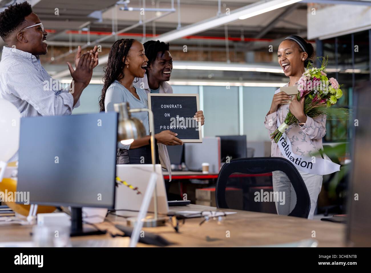Colleghi diversi che celebrano la promozione con fiori e firmano in un moderno ambiente da ufficio Foto Stock