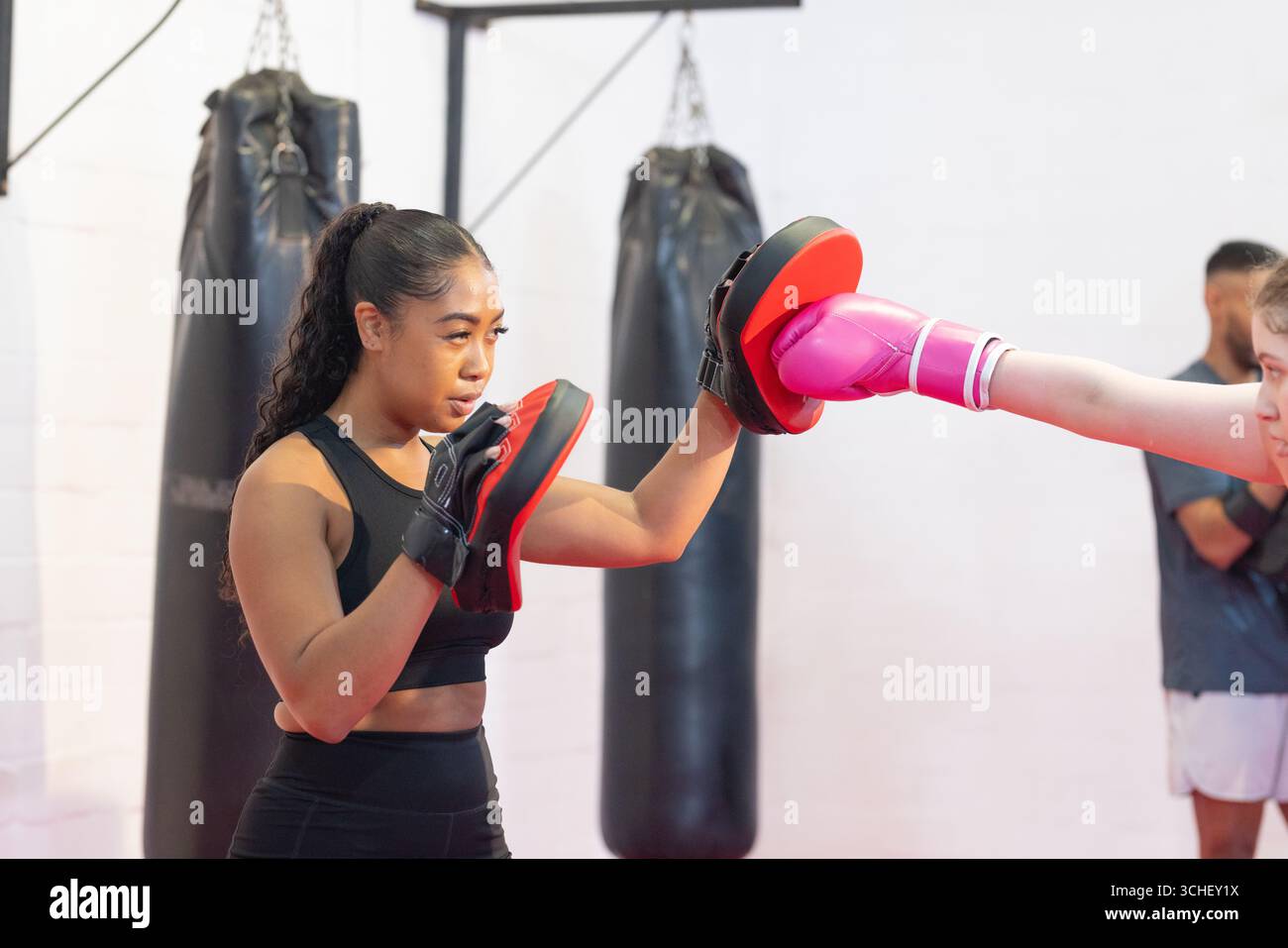 Istruttrice asiatica con guanti che guidano l'apprendista che puzza con guanti rosa nella palestra di pugilato Foto Stock