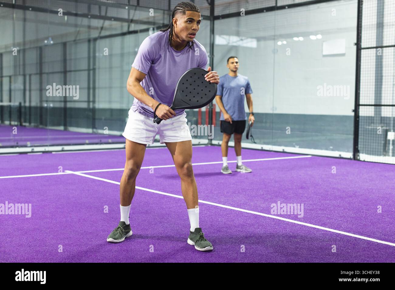 Diverse palette di posizionamento per coppie maschili su un campo da paddle tennis viola con linee bianche e pareti in vetro Foto Stock