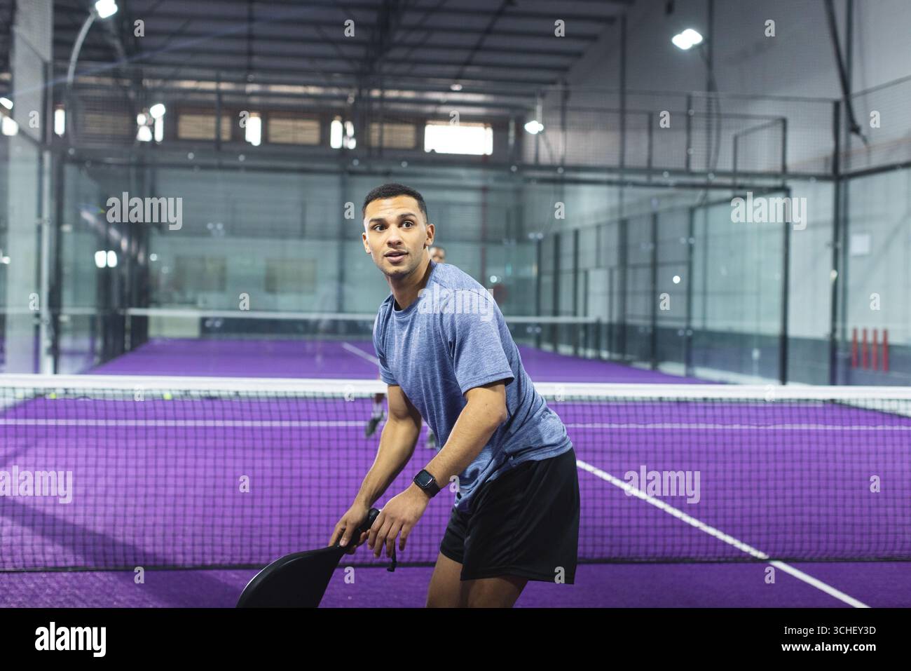 Uomo sportivo in piedi a rete sul campo viola in padel con racchetta e smartwatch Foto Stock