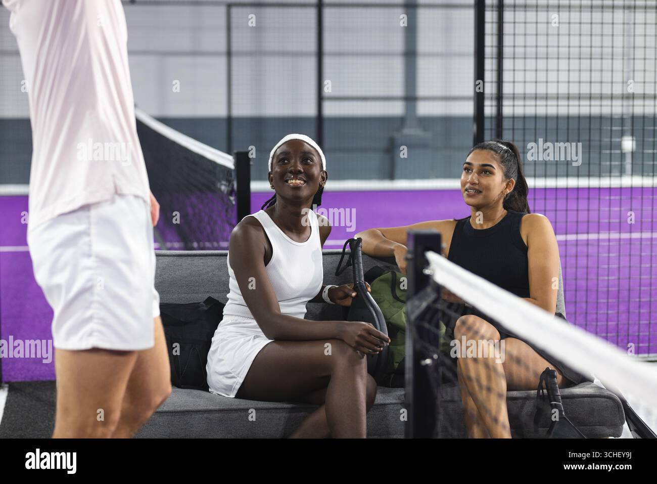 Diverse amiche che indossano abbigliamento sportivo seduto sulla panchina accanto alla rete con una borsa sportiva Foto Stock