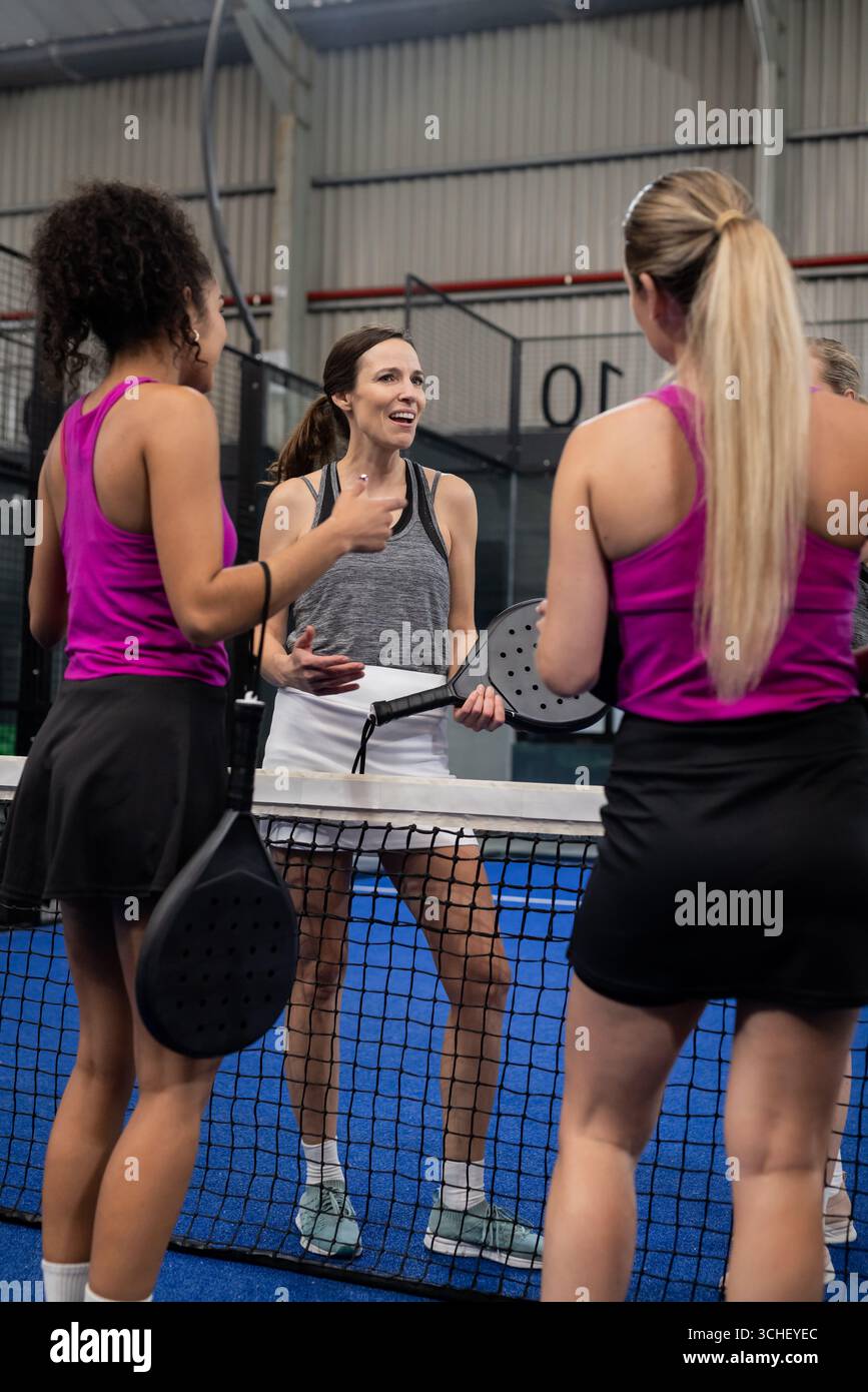 Diverse partner femminili in piedi sul campo di padel blu in erba con racchette sotto l'illuminazione superiore Foto Stock