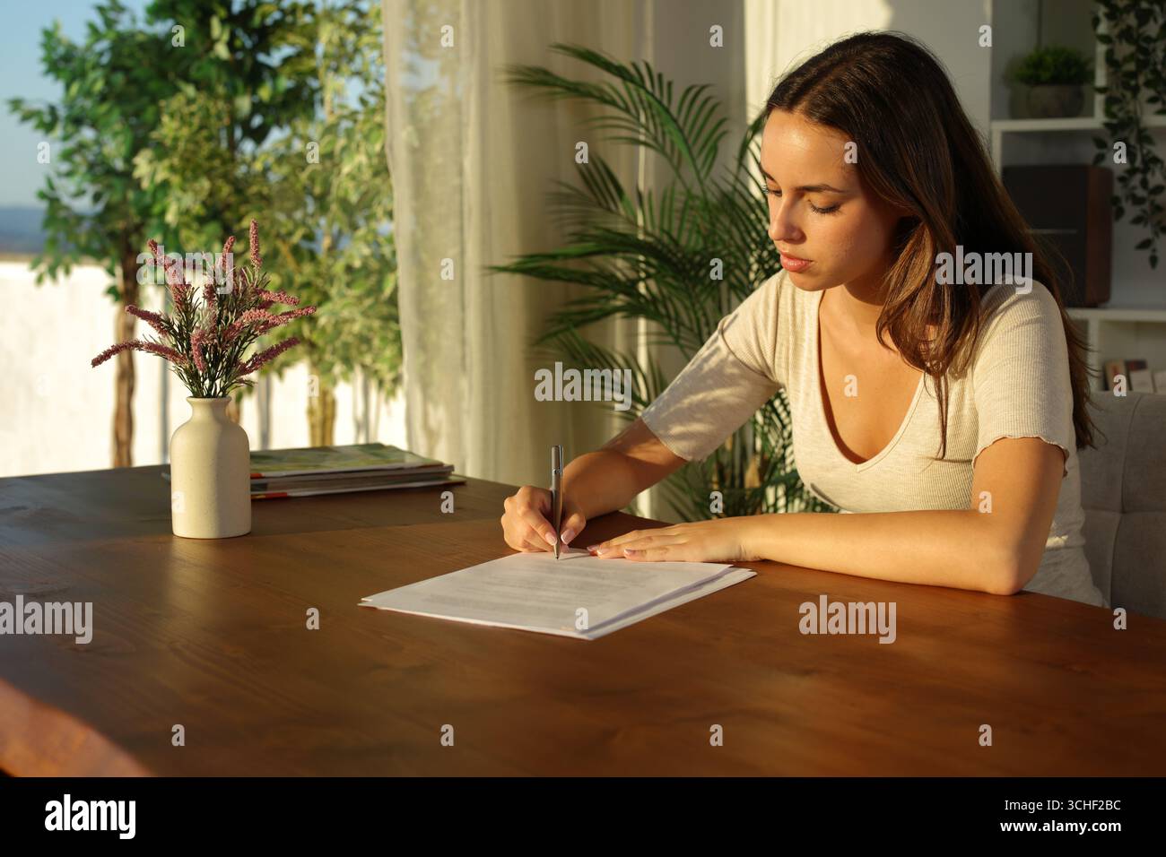 Donna a casa che firma un documento cartaceo al tramonto su un tavolo di legno Foto Stock
