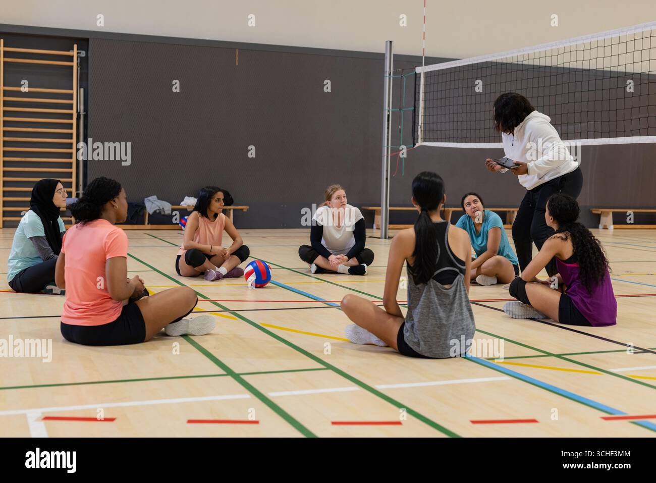 Diverse atlete di pallavolo che ascoltano l'allenatore che spiega le giocate in palestra con pallavolo Foto Stock