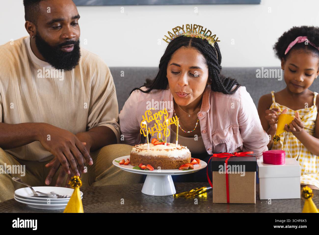 Festeggia il compleanno, donna che soffia candele sulla torta con la famiglia felice a casa Foto Stock