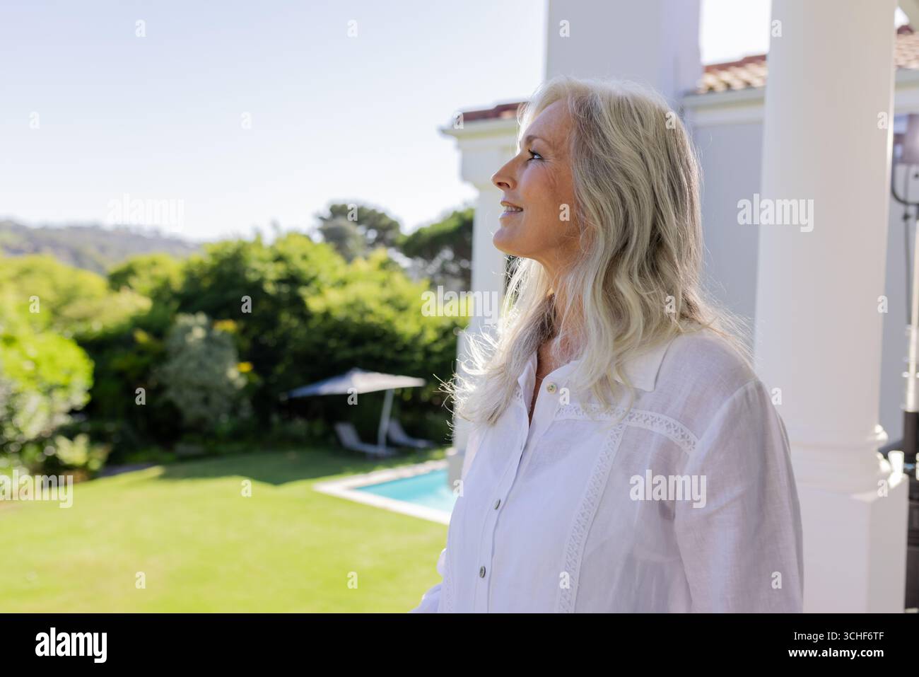 Donna anziana in piedi che guarda il prato verde dalla colonna del portico, con piscina e ombrello, spazio per fotocopie Foto Stock