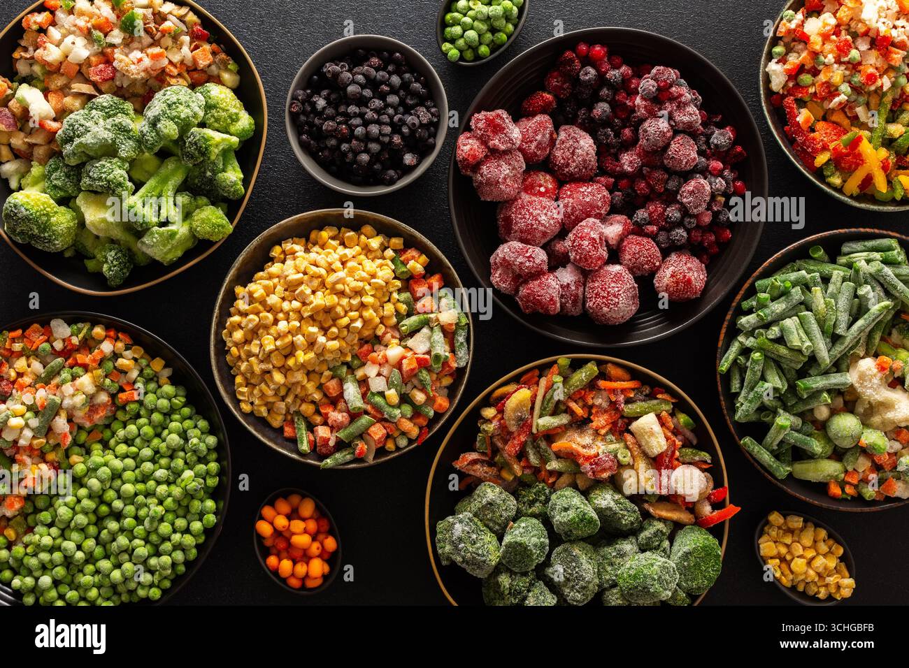 Una varietà di verdure e frutta congelate disposte in piatti, su sfondo scuro, catturando l'essenza della conservazione estiva per l'inverno Foto Stock