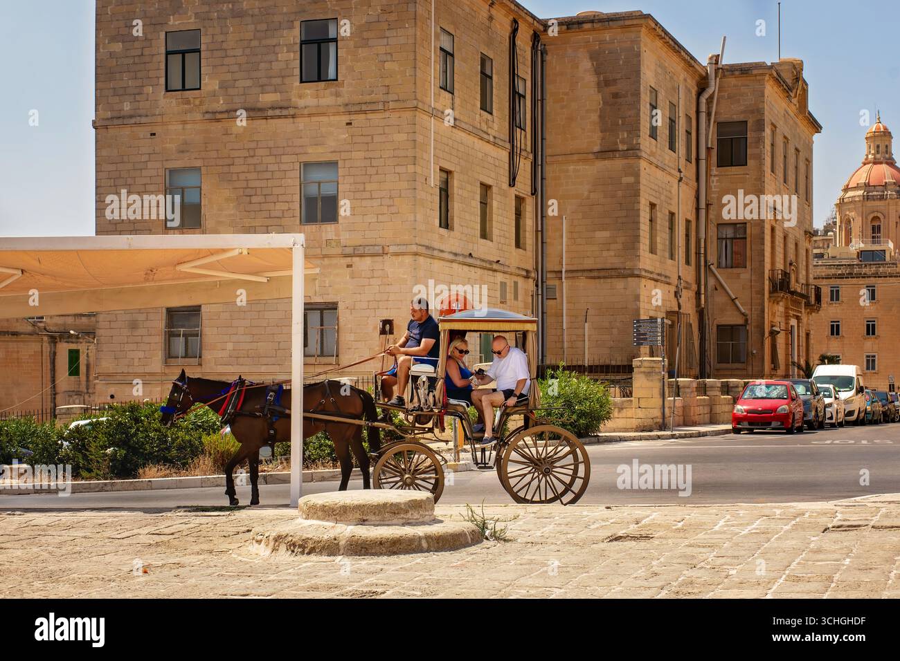 La Valletta, Malta - 31 agosto 2025: Tradizionale carrozza trainata da cavalli con turisti che passano davanti a vecchi edifici calcarei in una giornata di sole in un'Europa storica Foto Stock