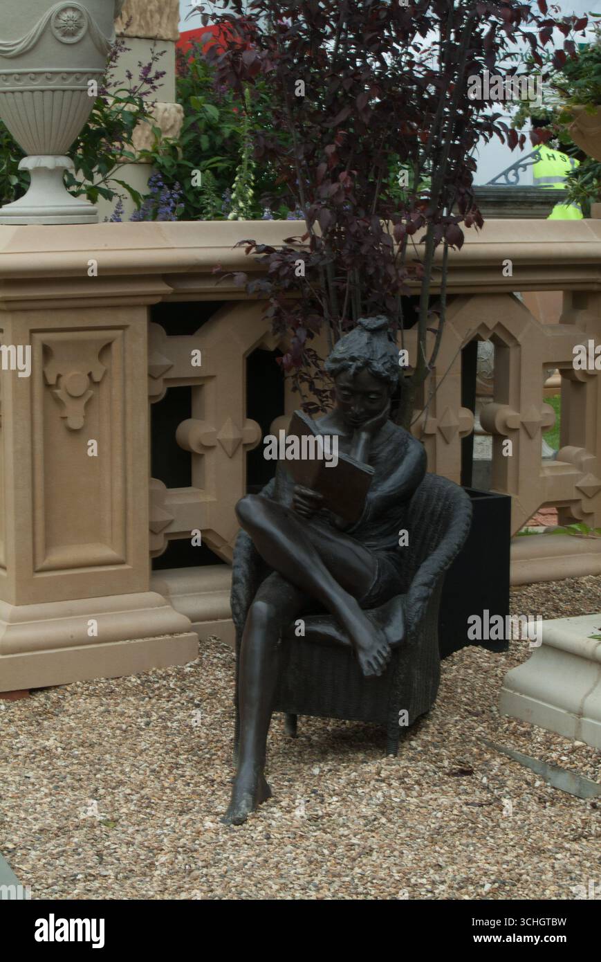 Una statua di bronzo raffigura una donna seduta e che legge un libro in un giardino splendidamente disposto con architettura ornamentale che la circonda. Foto Stock