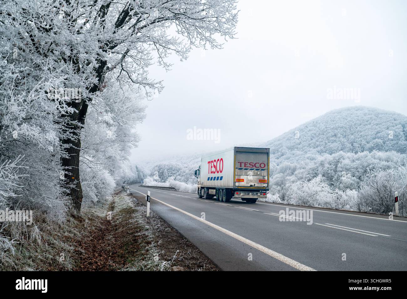NITRA, SLOVACCHIA, 12 DICEMBRE 2024: Tesco Truck percorre la strada innevata attraverso un paesaggio invernale bianco, fornendo cibo e rifornimenti Foto Stock