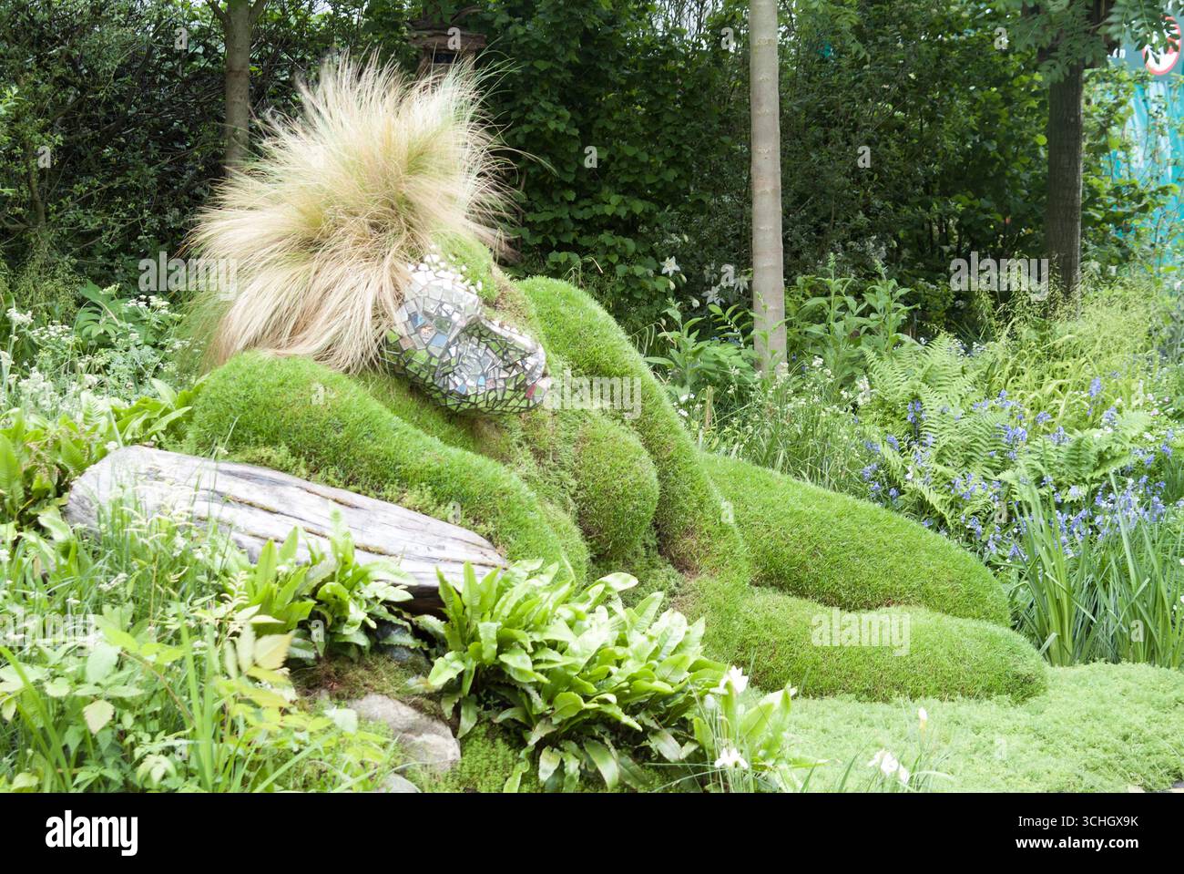 Una figura sdraiata realizzata in muschio riposa tra piante vivaci in un tranquillo giardino, che mostra l'arte e la creatività della natura. Foto Stock