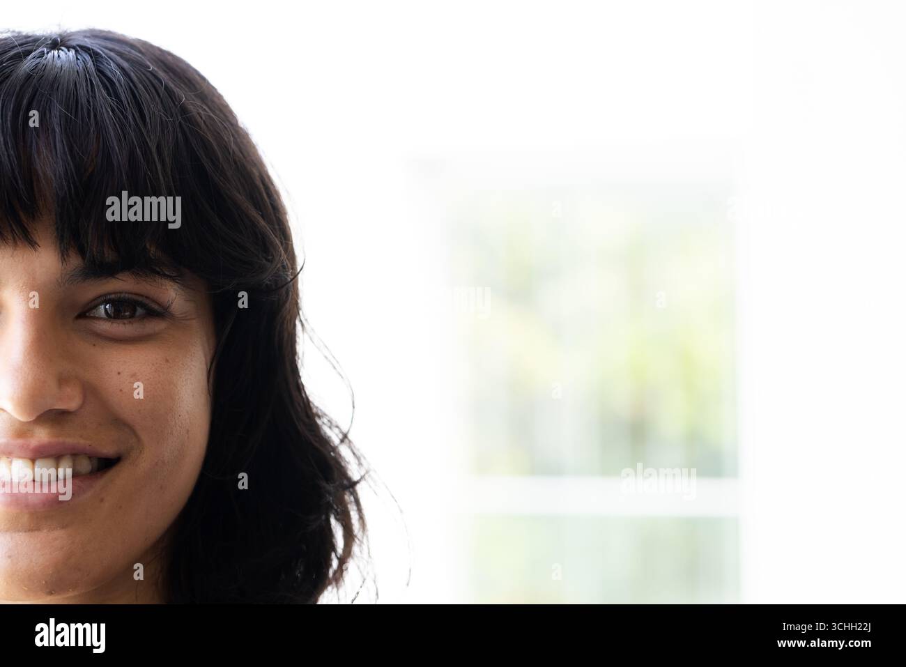 Donna sorridente con capelli scuri che gode di una luce naturale brillante in interni, a casa, spazio di copia Foto Stock