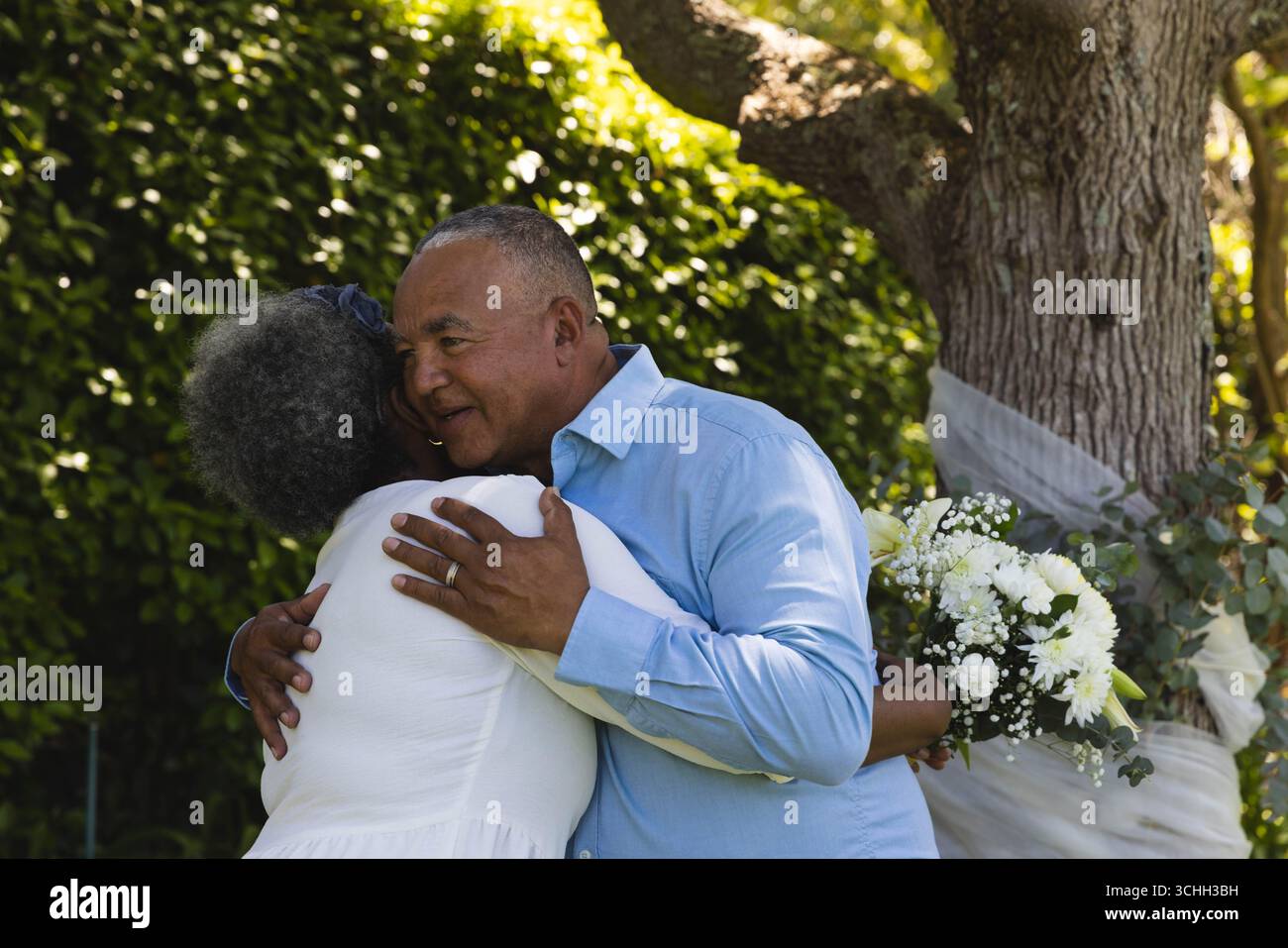 Al matrimonio, la coppia senior si abbraccia all'aperto, tenendo un bouquet di fiori bianchi Foto Stock