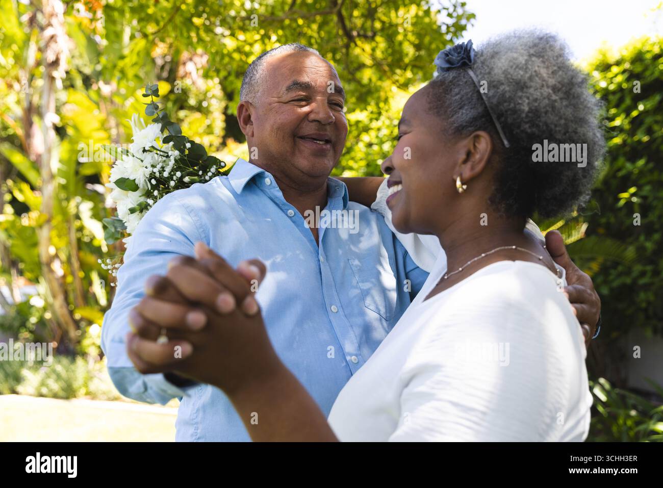 Al matrimonio, una coppia senior danzerà gioiosamente in giardino, abbracciando l'amore e la felicità insieme Foto Stock