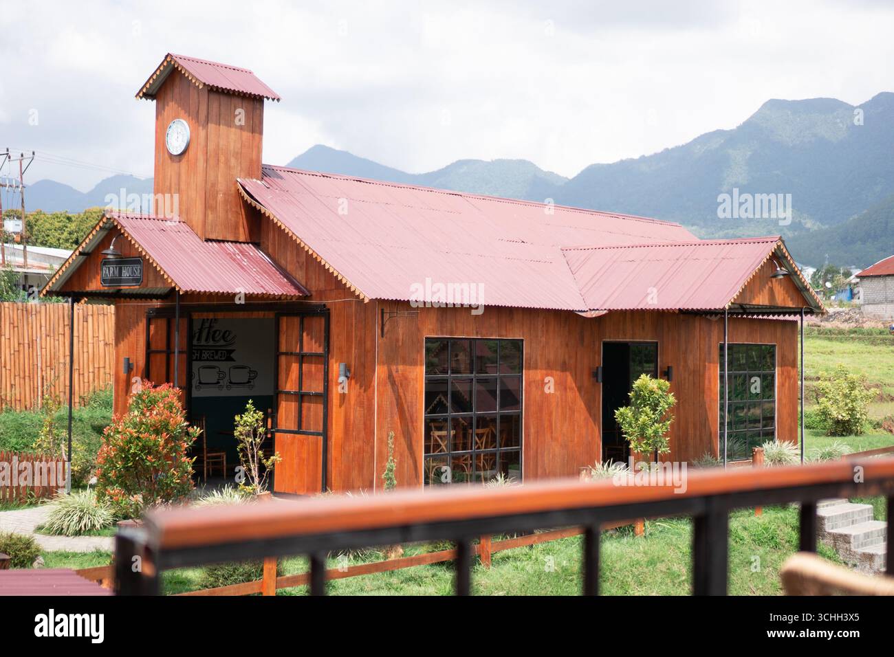 Caffetteria in legno in stile rustico con tetto rosso e torre dell'orologio, situata nel mezzo delle risaie con vista sulle montagne. Foto Stock
