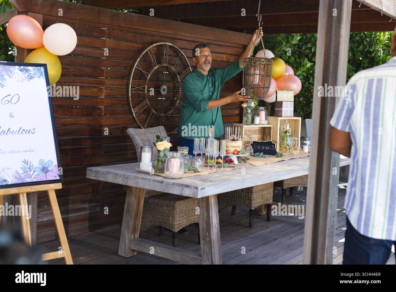Uomo che decora un tavolo da festa all'aperto con palloncini e bevande per festeggiare Foto Stock