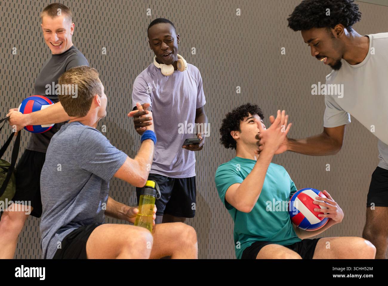 Diversi partner di pallavolo maschile che riposano nella sala dello sport con pallavolo e bottiglia d'acqua Foto Stock