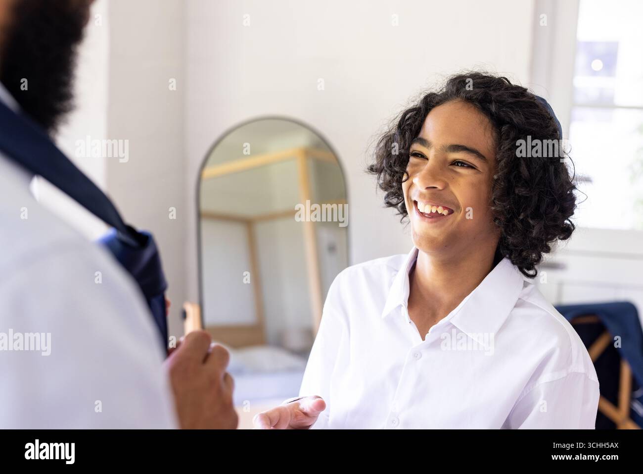 Famiglia variegata, figlio sorridente in camicia bianca che si prepara per le celebrazioni religiose a casa Foto Stock