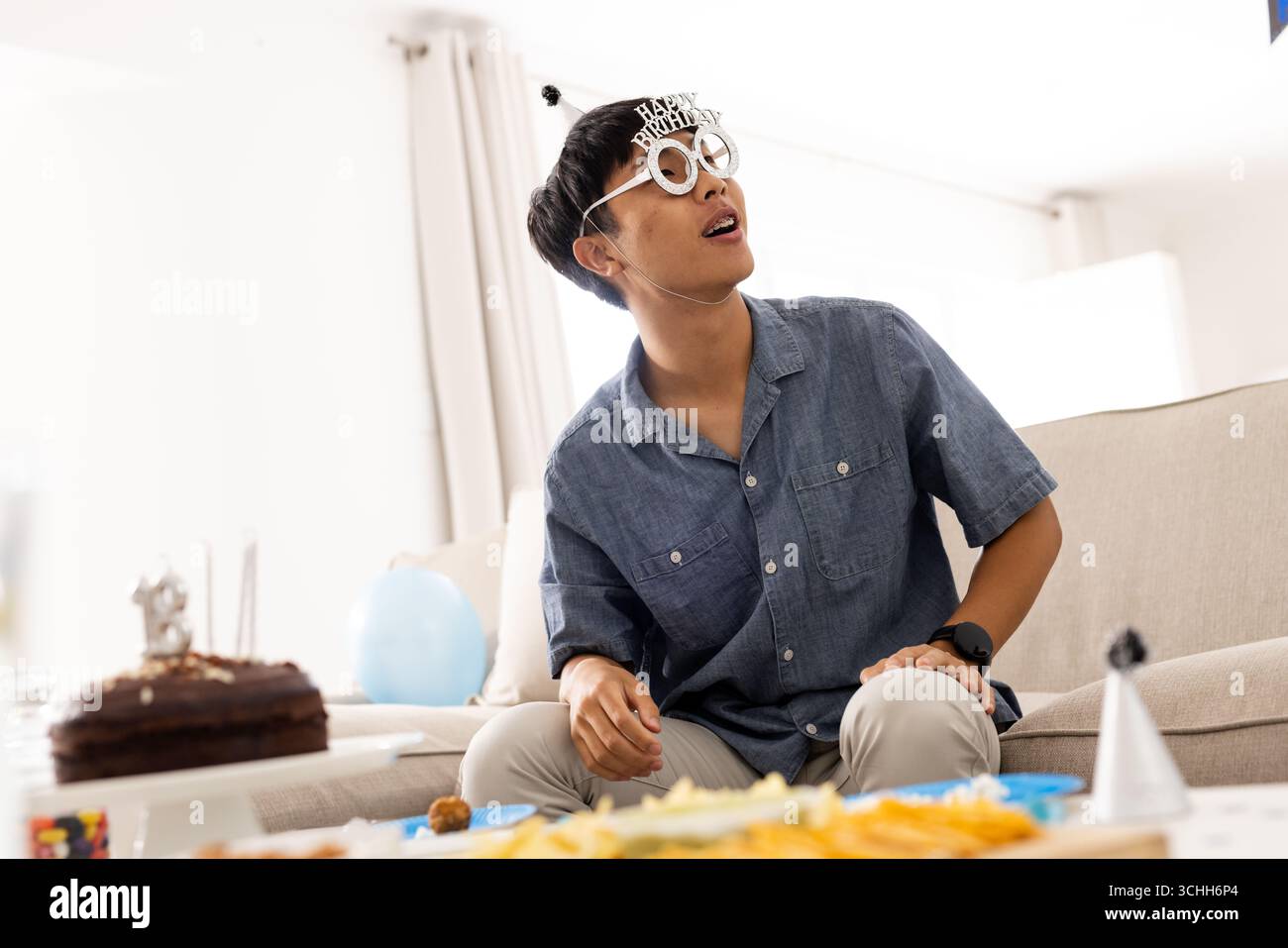 Festeggiamo il compleanno, uomo asiatico che indossa occhiali divertenti seduti con spuntini, a casa, spazio fotocopie Foto Stock