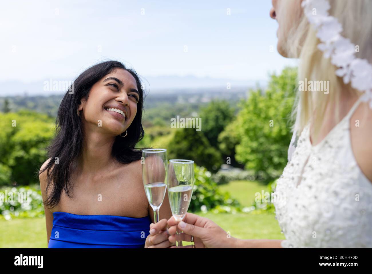 Donna sorridente in abito blu che brinda con la sposa all'aperto durante le celebrazioni nuziali Foto Stock