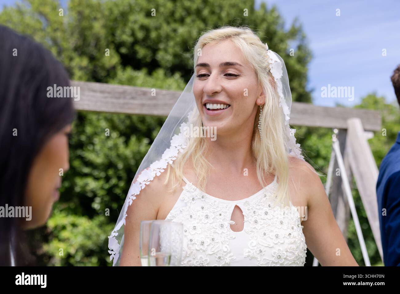 Sposa in elegante abito bianco sorridente mentre tiene un bicchiere di champagne all'aperto Foto Stock