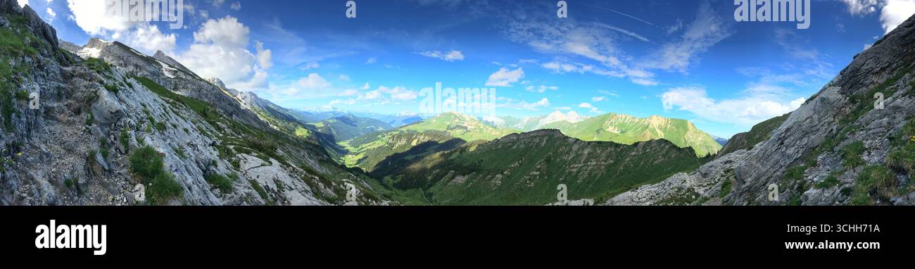 Paesaggio panoramico mozzafiato di lussureggianti valli verdi, pendii rocciosi di montagna e un sereno cielo blu. Ideale per l'uso come immagine di sfondo o di intestazione in Foto Stock