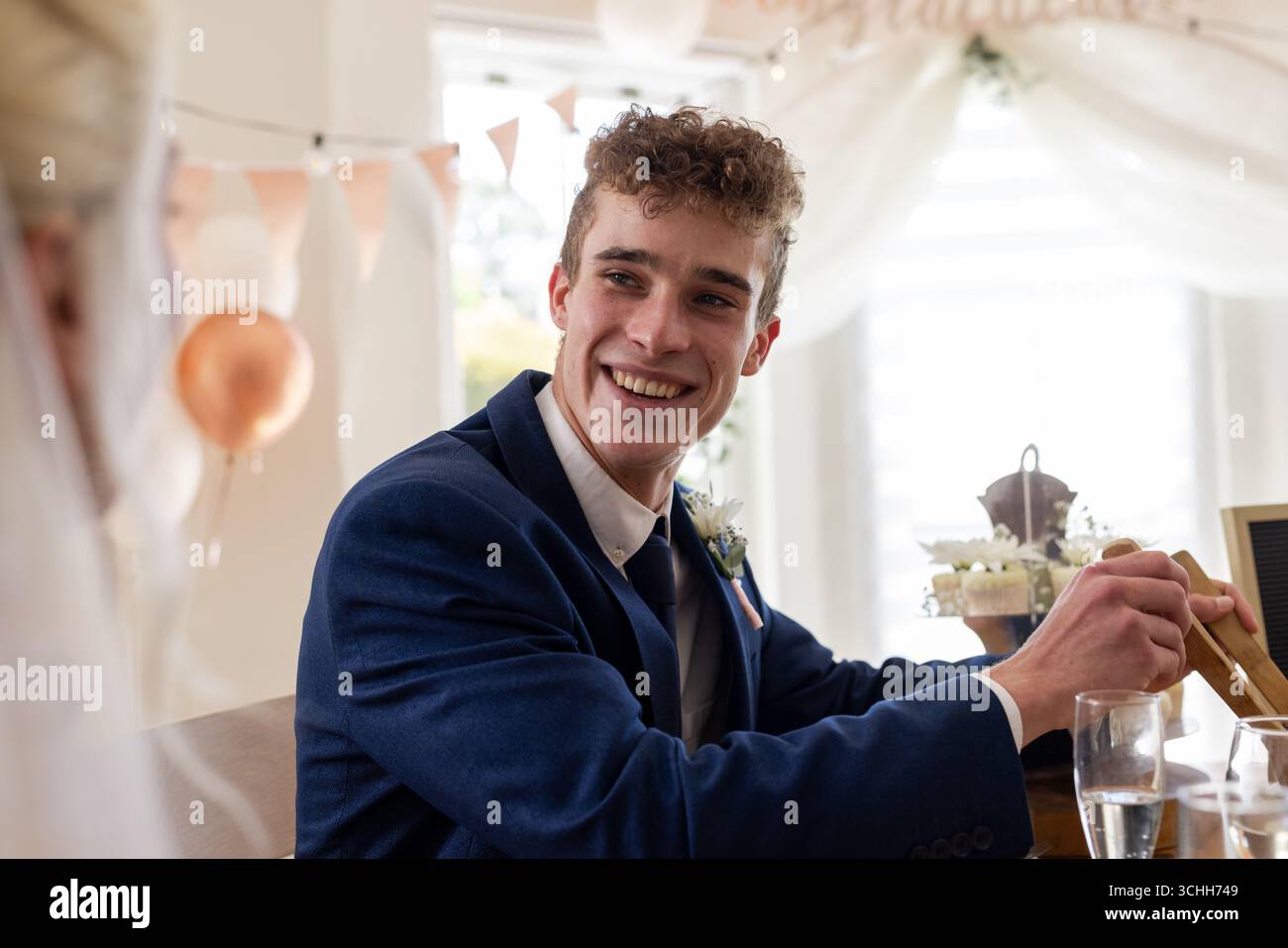 Spennellate in abito blu sorridendo gioiosamente durante il ricevimento di nozze in un luogo decorato Foto Stock