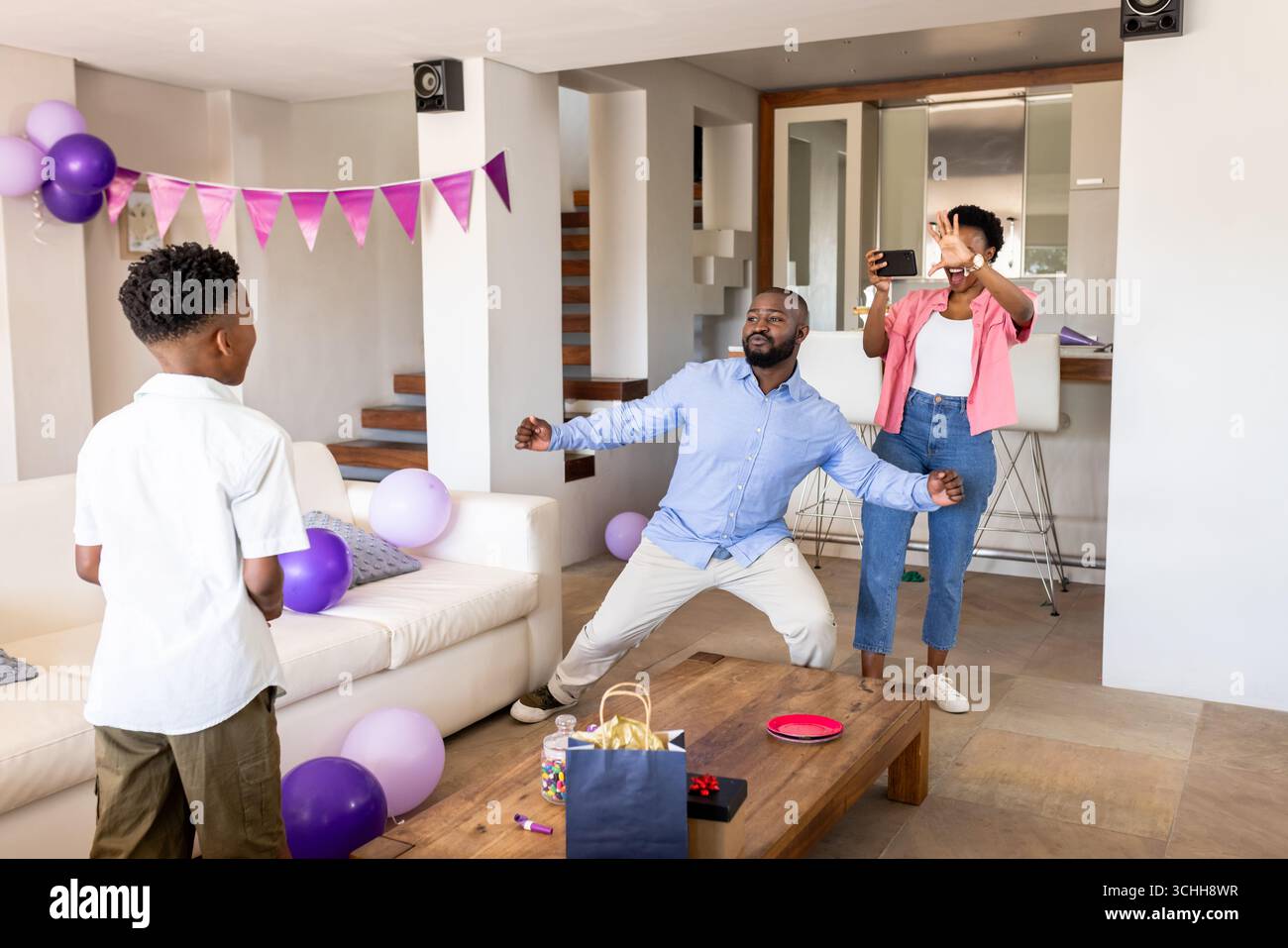Alla festa, festeggiando il compleanno a casa, padre afroamericano che balla, madre che scatta foto Foto Stock