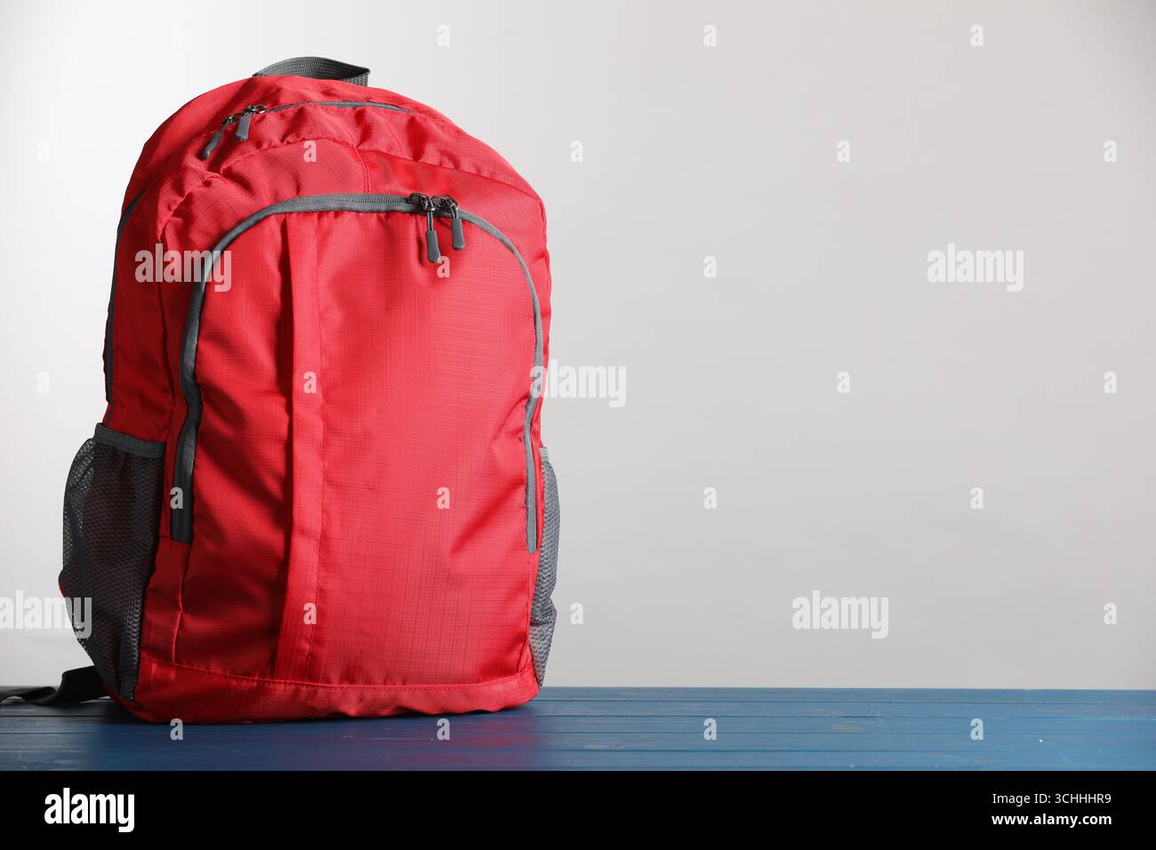 Zaino scolastico rosso su tavolo in legno blu su sfondo grigio chiaro, spazio per testo Foto Stock